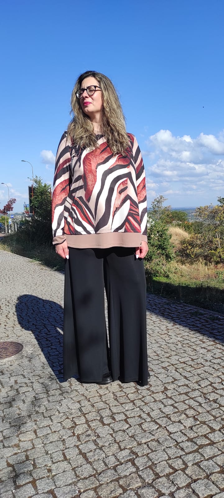 Mulher com blusa estampada castanha e preta e calças pretas largas num passeio ao ar livre