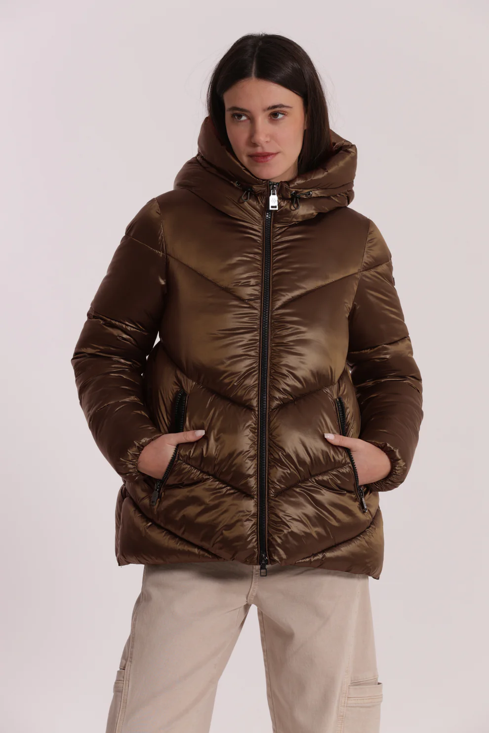 Casaco acolchoado castanho com capuz e bolsos, usado por mulher com calças bege