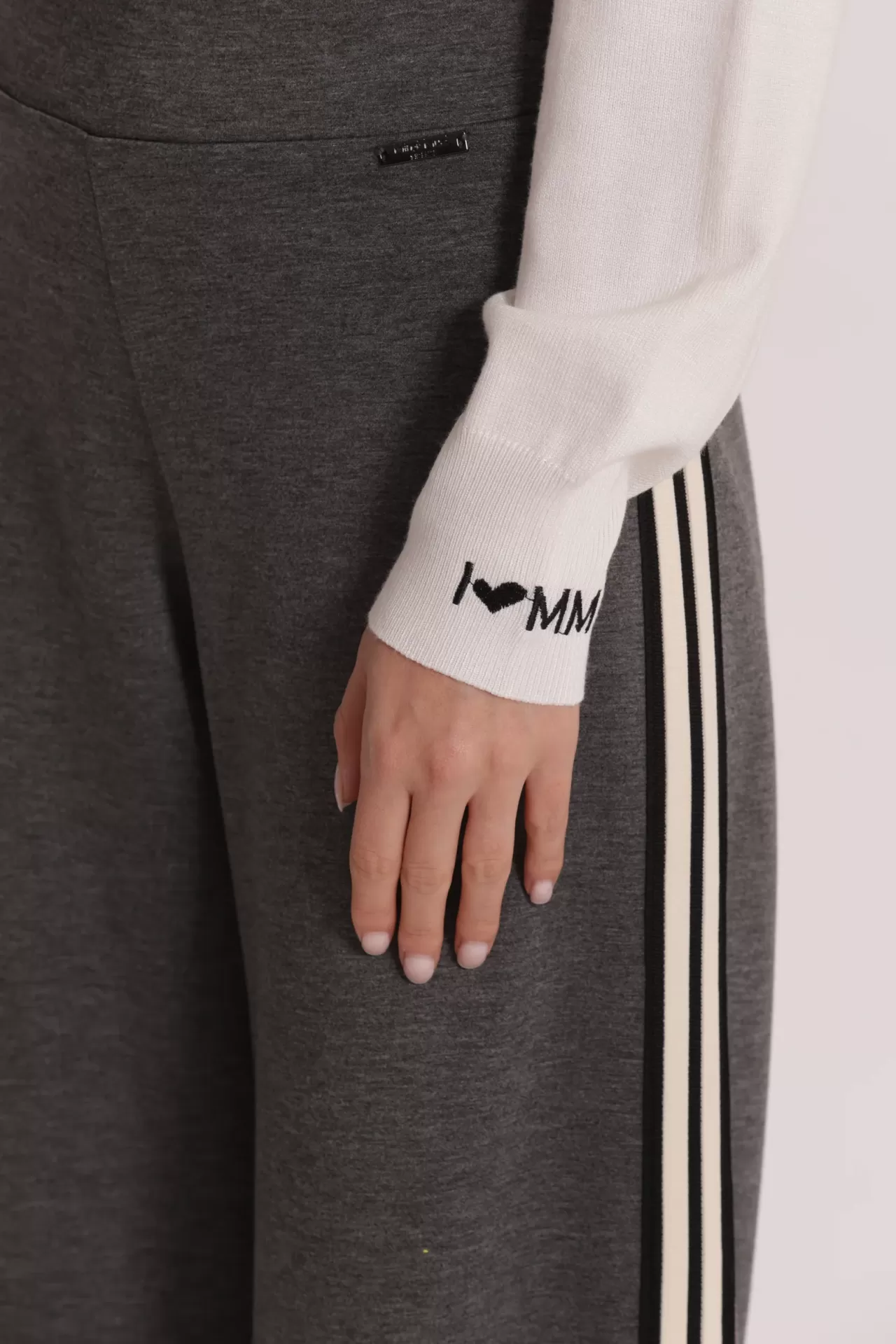 Manga branca de camisola com texto bordado e calças cinzentas com riscas laterais pretas e branco creme
