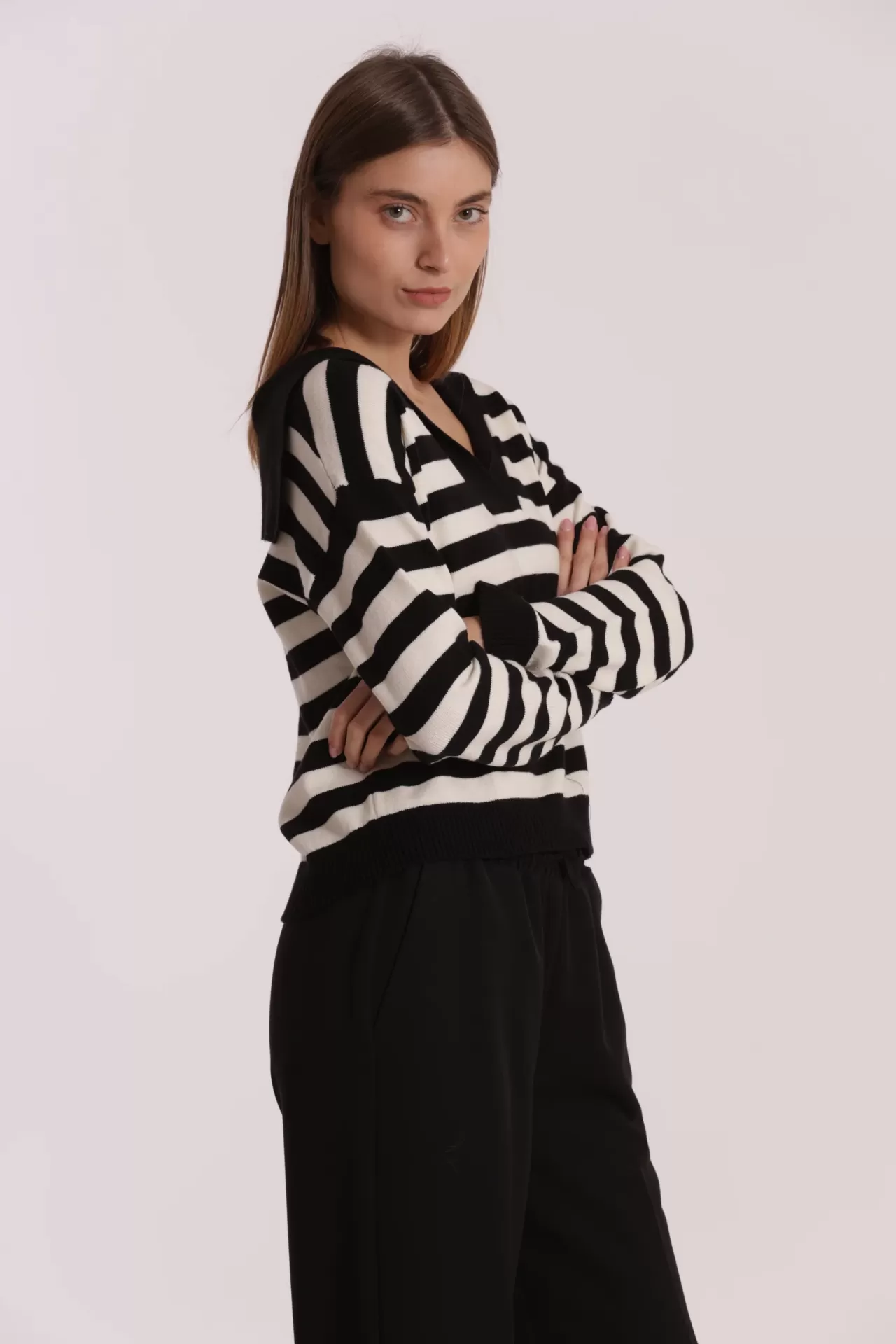 Mulher vestindo camisola riscada preta e branca com decote em V e calças pretas.