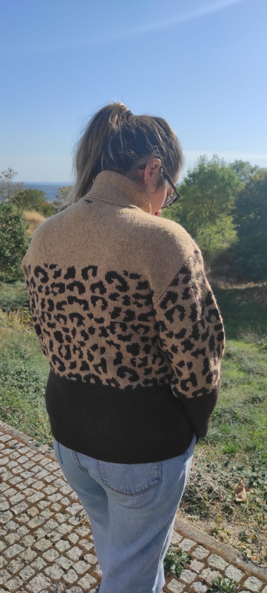Mulher de costas a usar camisola de malha com estampa animal print e gola alta ao ar livre