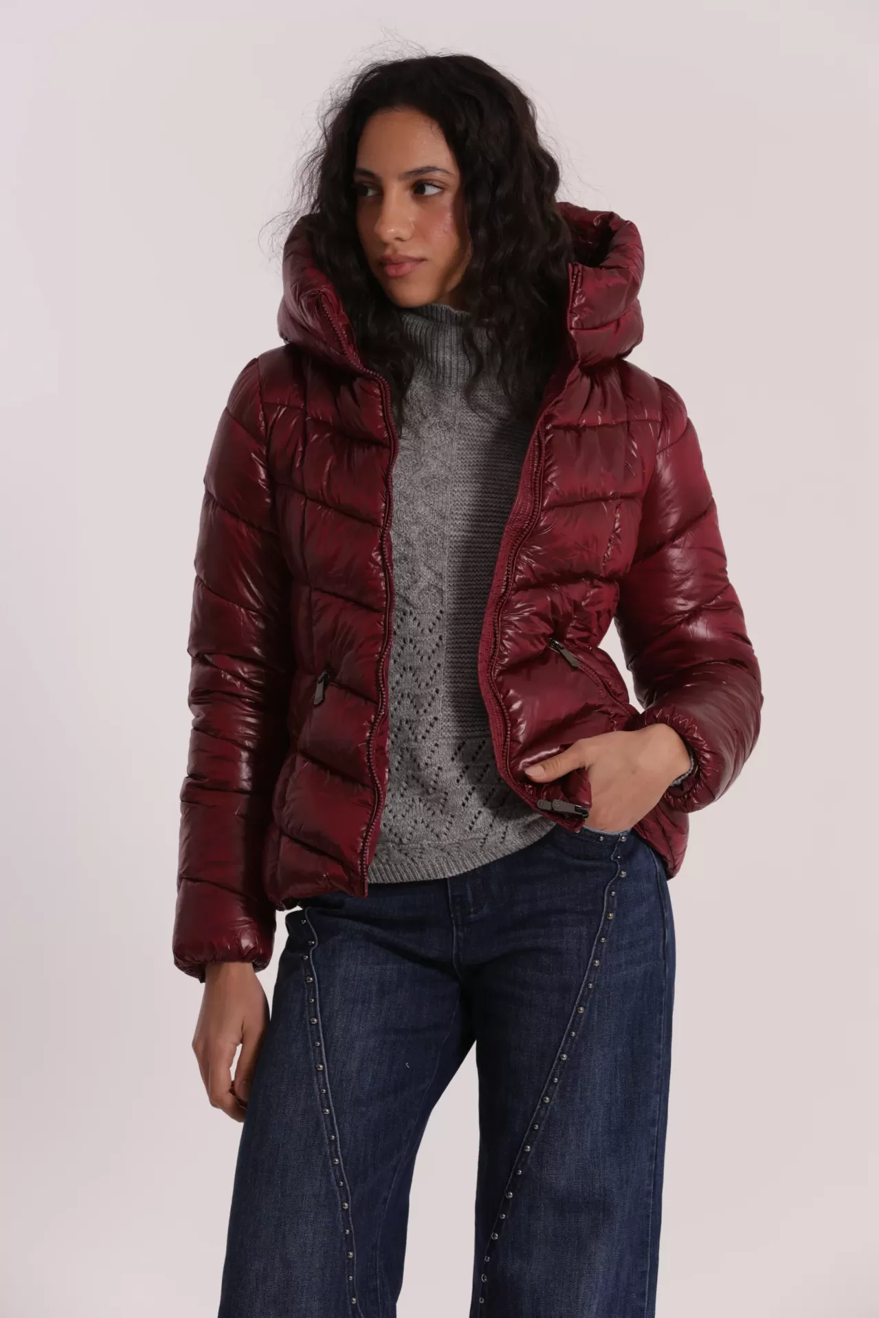 Casaco acolchoado vermelho vinho com capuz, camisola cinza e jeans com tachas