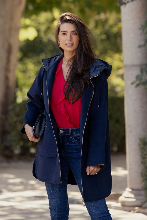Mulher com casaco azul escuro, blusa vermelha e calças de ganga ao ar livre