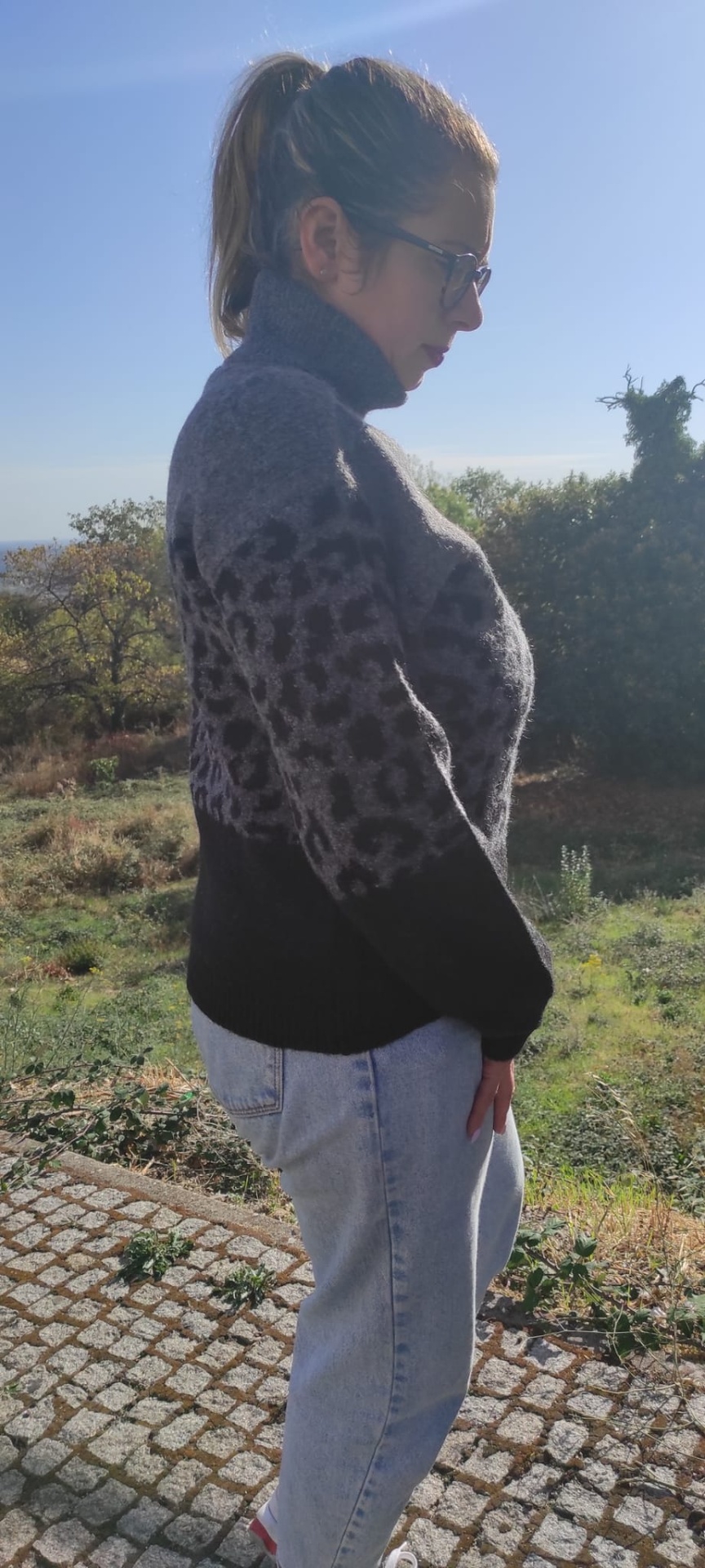 Mulher com camisola de padrão de leopardo cinzento e preto e calças de ganga num ambiente exterior