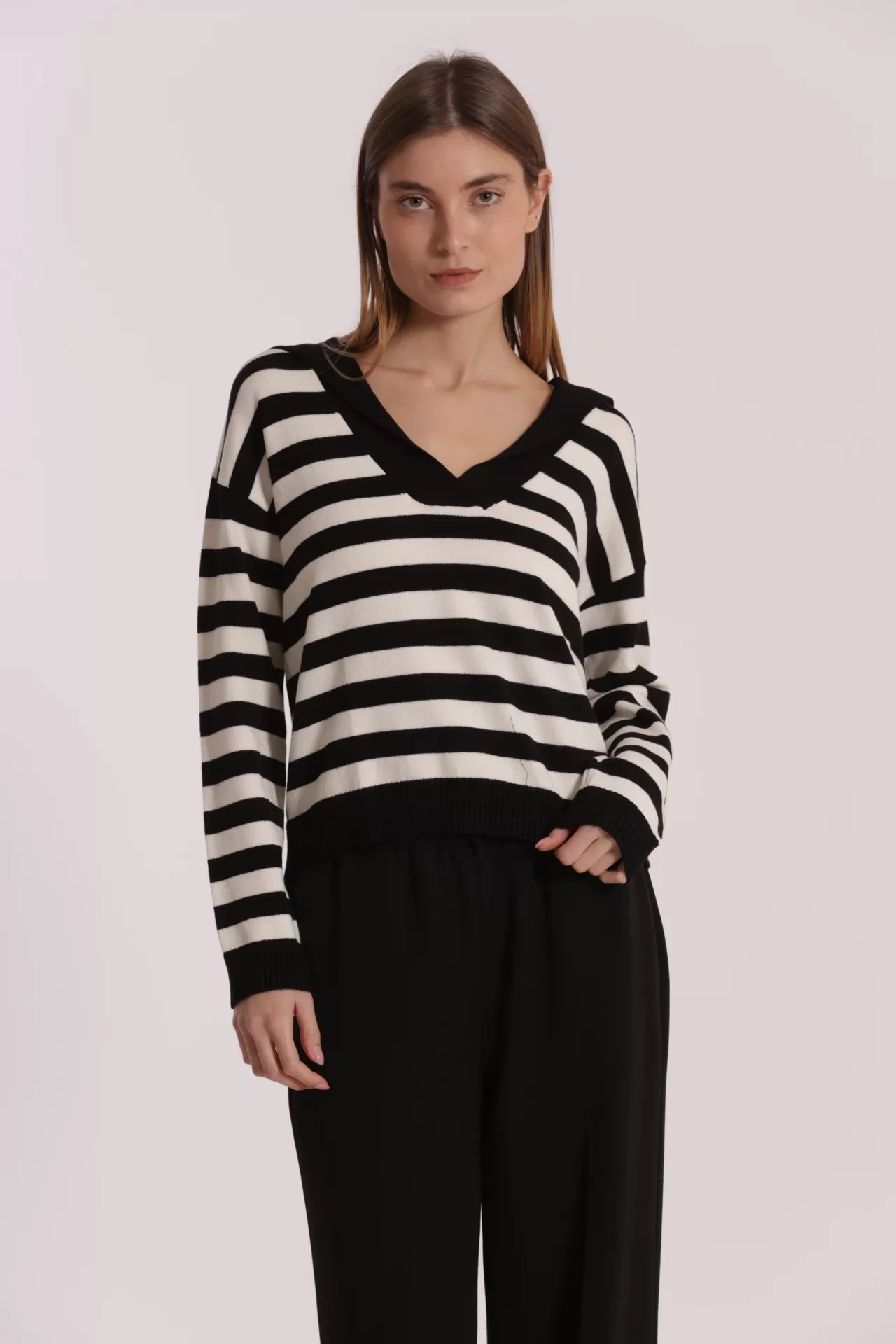 Mulher a vestir sweater riscas preto e branco com gola em V e calças pretas