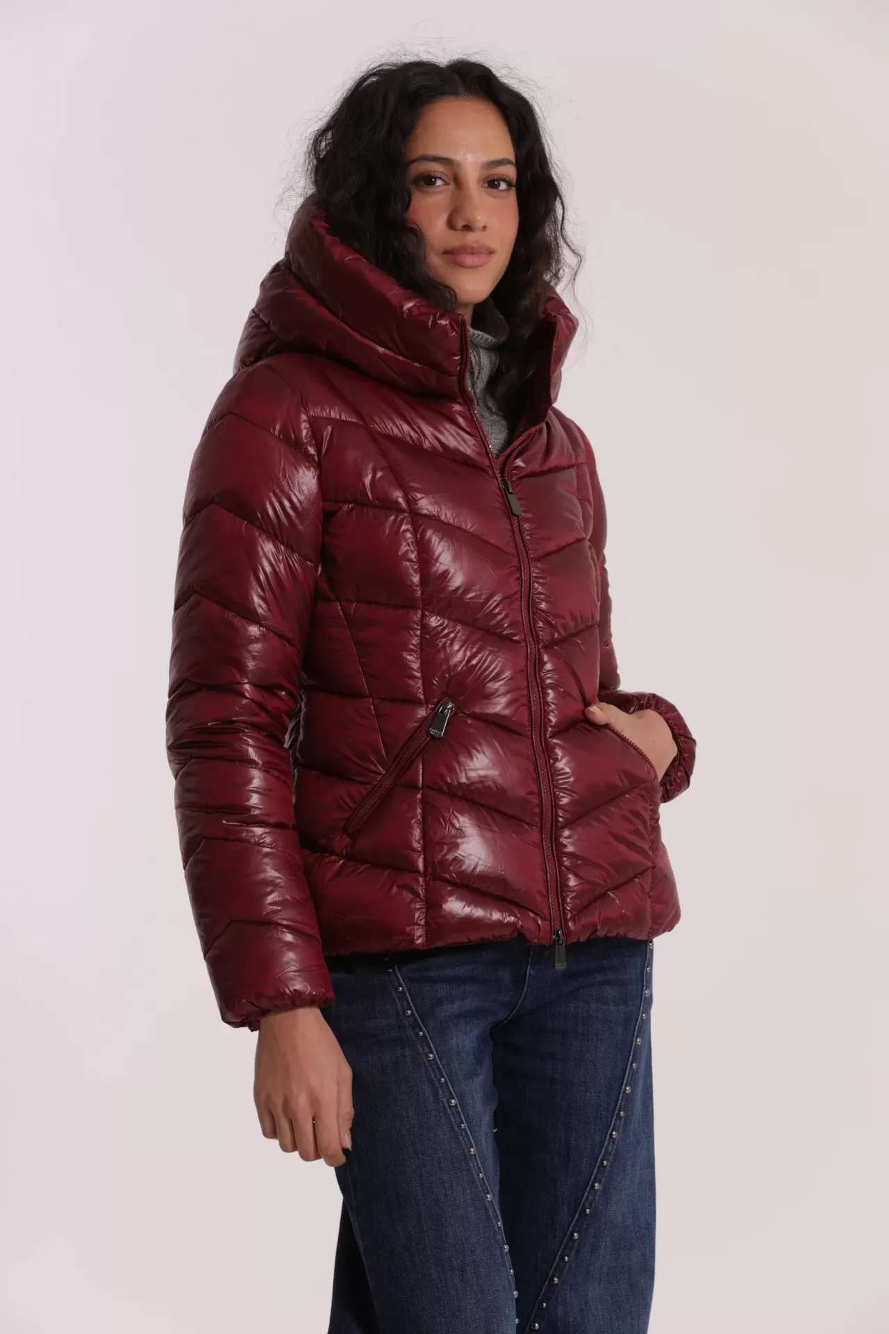 Casaco acolchoado bordô com capuz e fecho frontal, jeans azuis com tachas