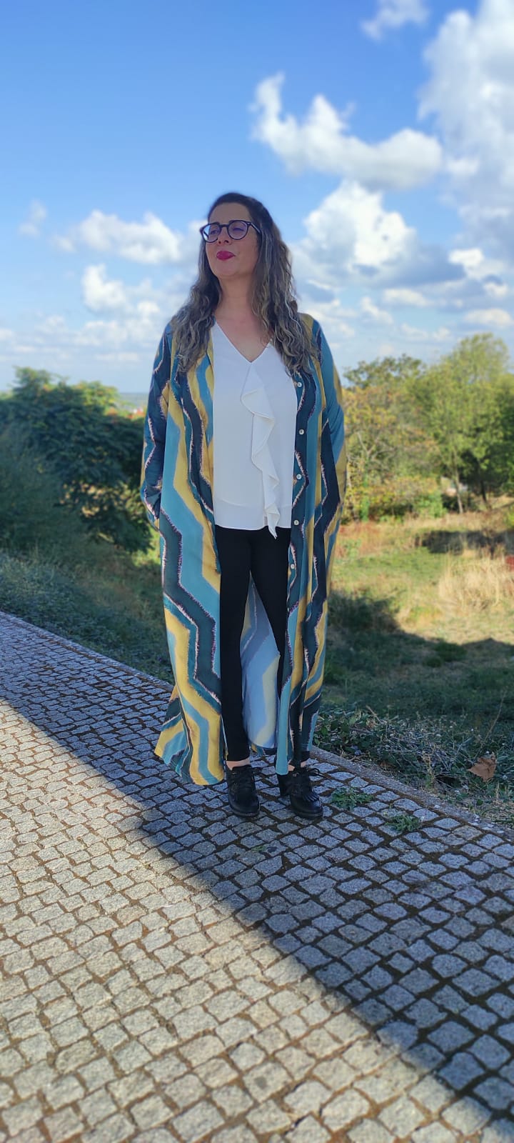 Mulher com casaco estampado, blusa branca e calças pretas ao ar livre