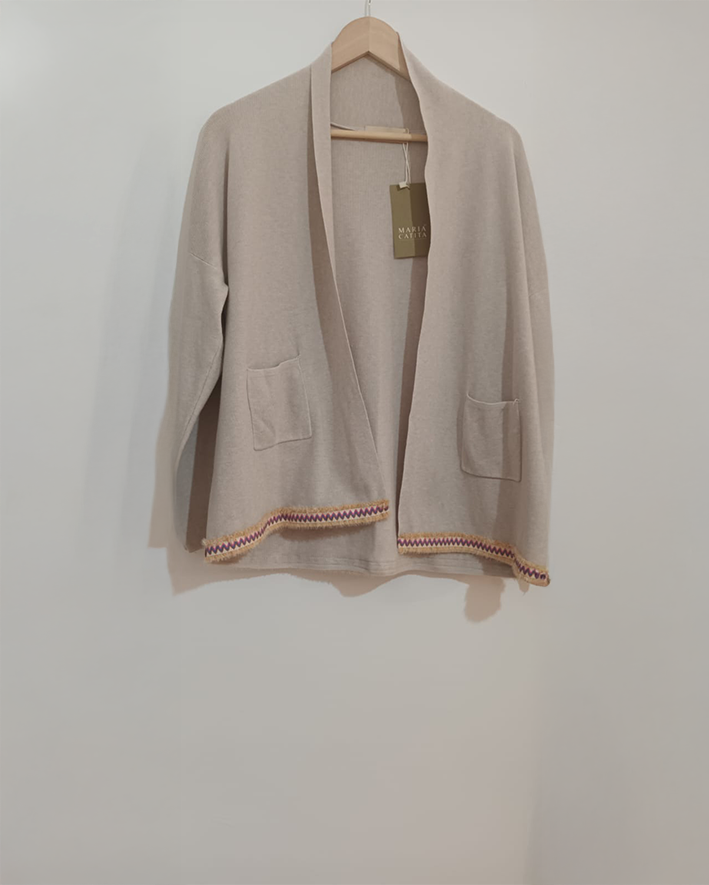 Casaco bege com bolsos e barra decorada pendurado num cabide de madeira.