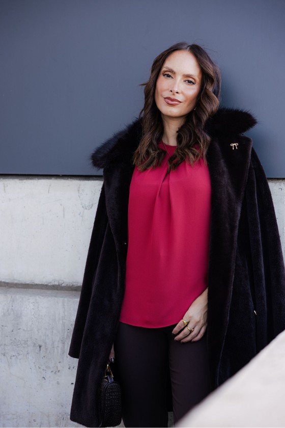 Mulher com casaco preto de pêlo e blusa magenta numa parede cinzenta