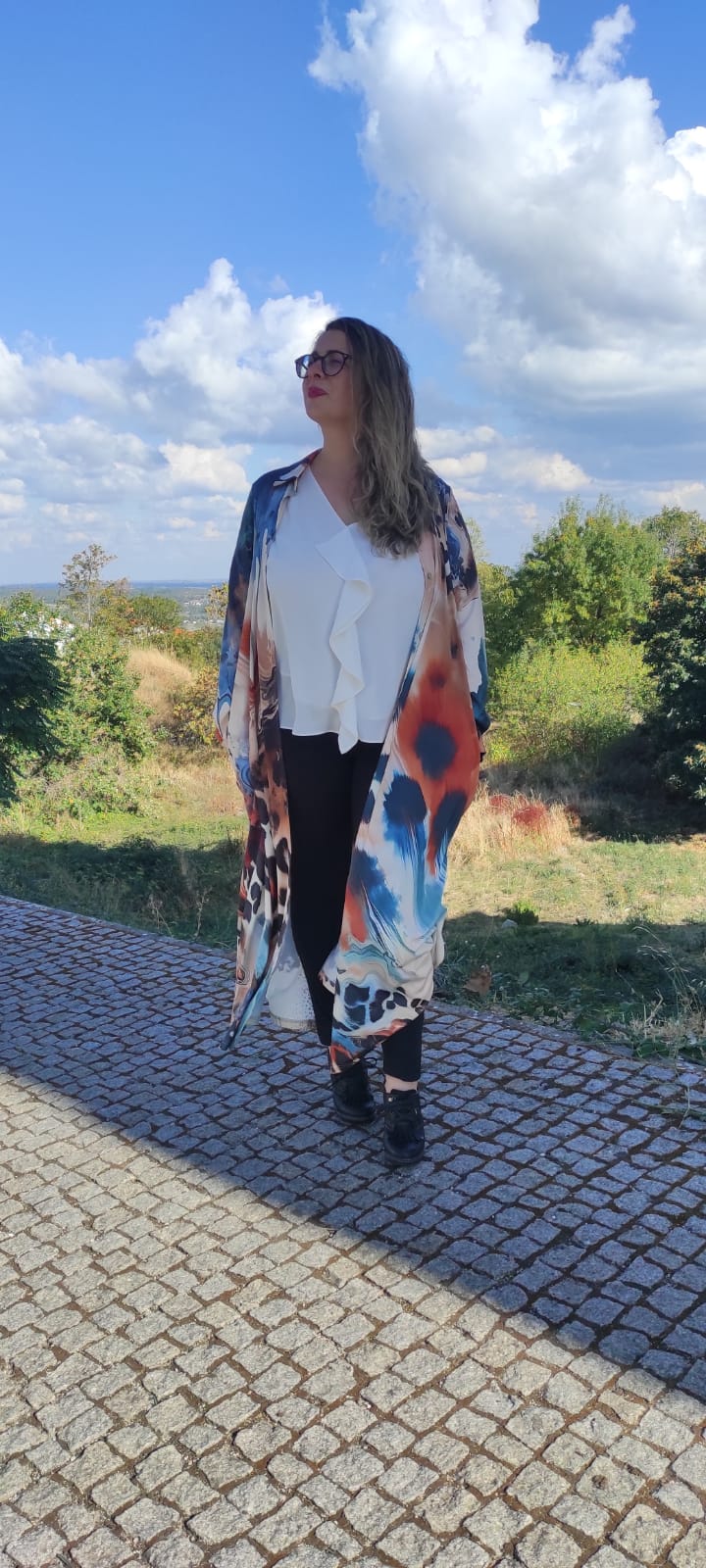 Mulher com kimono estampado colorido e blusa branca, em calçada portuguesa exterior