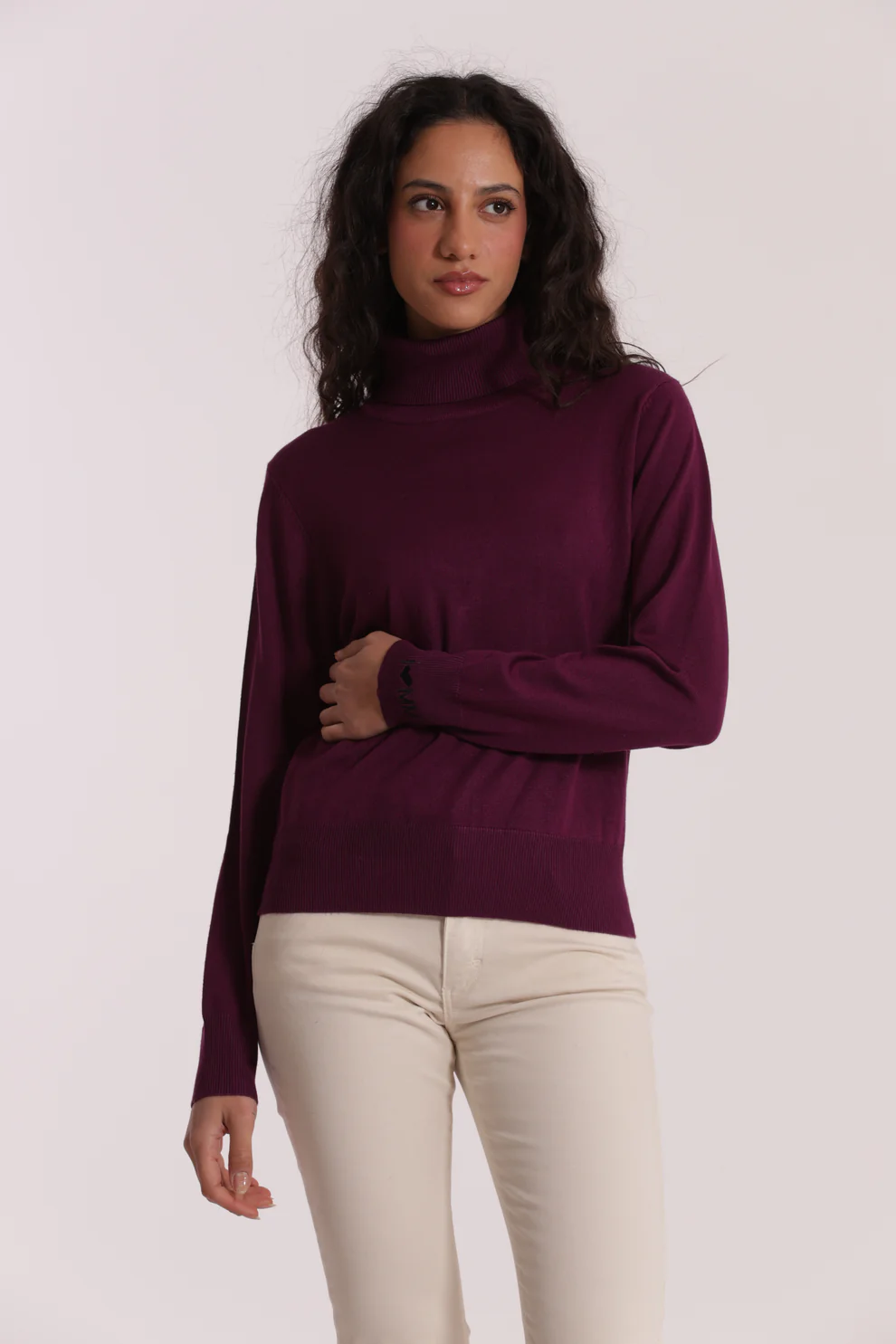 Mulher de cabelo escuro com camisola de gola alta vinho e calças claras