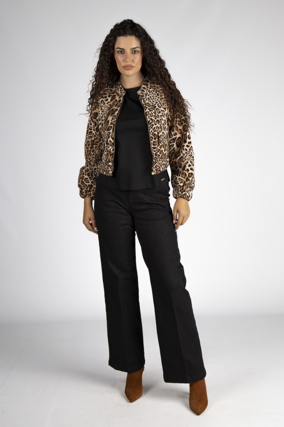 Mulher com casaco animal print, camisola preta, calças pretas e botas castanhas em fundo cinzento