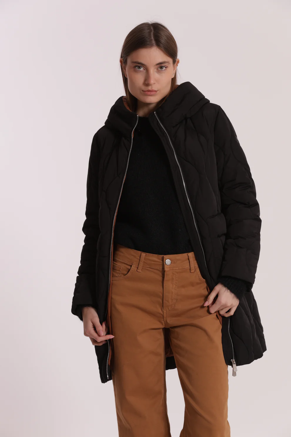 Mulher com casaco acolchoado preto, camisola preta e calças castanhas