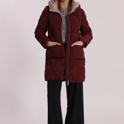 Casaco acolchoado bordeaux com capuz e bolsos, usado por mulher com calças pretas e botas castanhas.