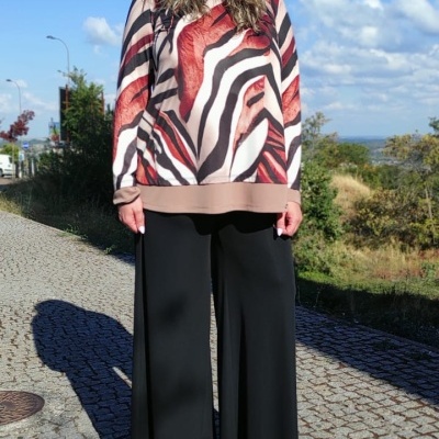 Mulher com blusa estampada abstrata e calças pretas largas ao ar livre