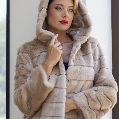 Casaco de pele bege com capuz e botões, usado por mulher.