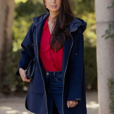 Mulher com casaco azul escuro, blusa vermelha e calças de ganga ao ar livre