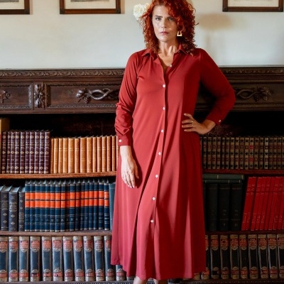 Vestido longo vermelho com botões e sapatos brancos de salto em biblioteca com estante de livros.