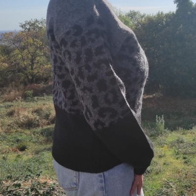 Mulher com camisola de padrão de leopardo cinzento e preto e calças de ganga num ambiente exterior