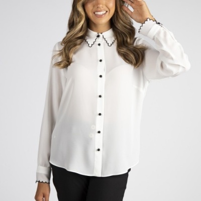 Mulher a usar camisa branca com botões pretos e gola com borda ondulada preta