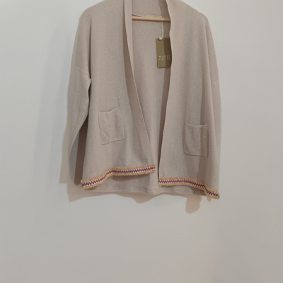 Casaco bege com bolsos e barra decorada pendurado num cabide de madeira.