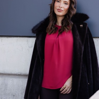 Mulher com casaco preto de pêlo e blusa magenta numa parede cinzenta