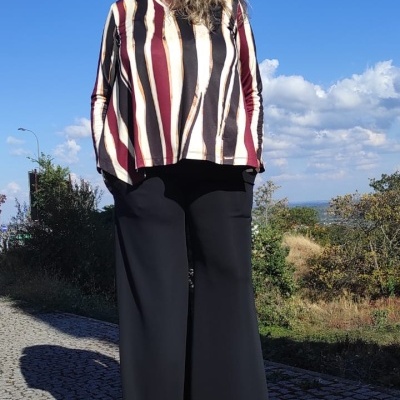 Mulher com blusa riscada castanha e vinho e calças pretas largas ao ar livre