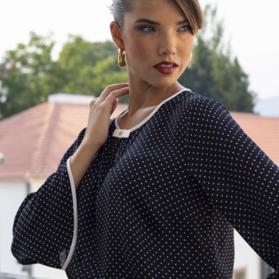 Blusa preta de pontos brancos com detalhe branco na gola e punhos, combinada com roupa vermelha com botões dourados.