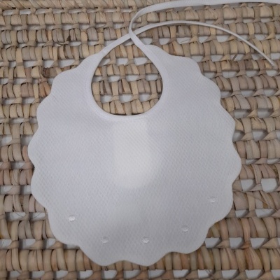 Babete branco em tecido com bordas onduladas sobre superfície de ráfia entrelaçada