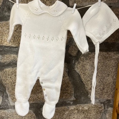 Conjunto de bebé branco em malha com macacão e casaco pendurado num varal