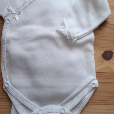 Body de bebé branco com mangas compridas e fecho de pressão sobre superfície de madeira