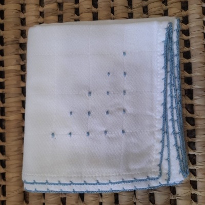 Lenço branco com bordado azul sobre superfície trançada bege