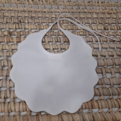 Babete de bebé branco com bordas onduladas sobre superfície de palha entrelaçada