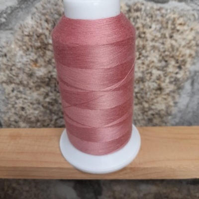 Cone de linha rosa antigo em base branca sobre tábua de madeira com parede de pedra ao fundo