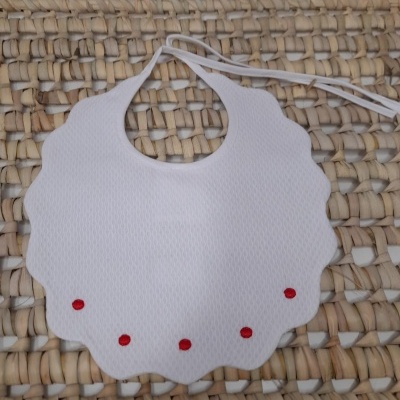 Babete branco com textura ondulada e detalhes vermelhos, sobre superfície trançada