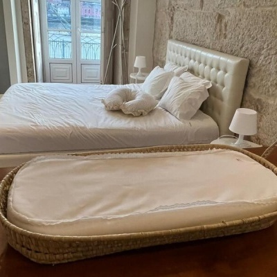 Quarto com cama estofada creme, candeeiros brancos e cesto de fibra natural com almofada branca