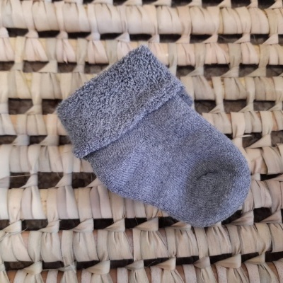 Meia bebé cinzenta sobre superfície de palha entrelaçada