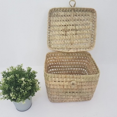 Caixa quadrada de verga com tampa aberta ao lado de vaso com planta artificial