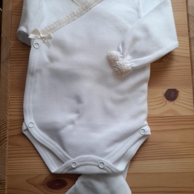 Body de bebé branco com renda creme e pé integrado sobre madeira clara