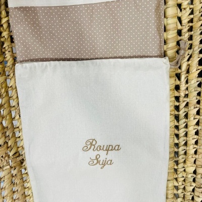 Sacola de tecido branca para roupa suja com interior bege com bolinhas colocada sobre palha trançada