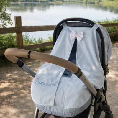 Carrinho de bebé azul claro com cobertura e nome Francisco bordado, num caminho junto a lago