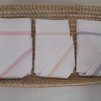 Três fraldas brancas com bordas coloridas dentro de um cesto de palha