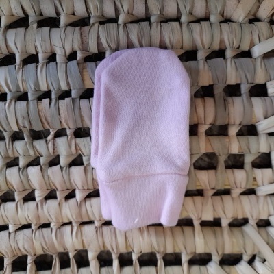 Luva de bebé rosa clara sobre superfície trançada natural