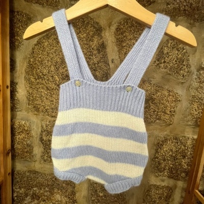 Macacão de bebé às riscas azuis e brancas, com alças, pendurado numa cabide de madeira