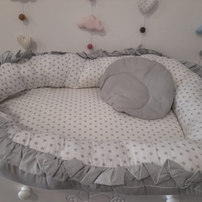 Berço portátil branco com estrelas cinzentas e almofada redonda cinzenta em cima de cômoda branca