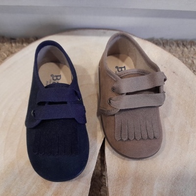 Dois sapatos infantis tipo mocassim em azul escuro e bege sobre madeira clara