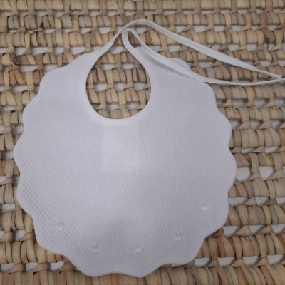 Babete texturizado branco com tiras ajustáveis sobre superfície de palha