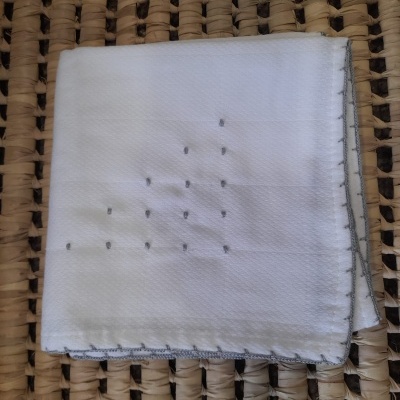 Lenço branco com bordados e costura cinzenta sobre tecido trançado