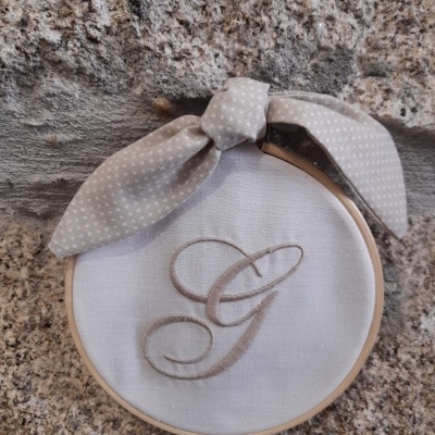 Aparador de bordado branco com letra G bordada e fita bege com pontos brancos