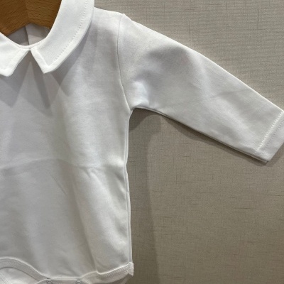 Body de bebé branco com gola e mangas compridas pendurado num cabide